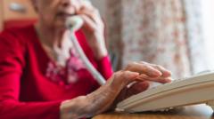 Elderly woman speaking on a traditional landline phone, looking concerned about digital switchover.